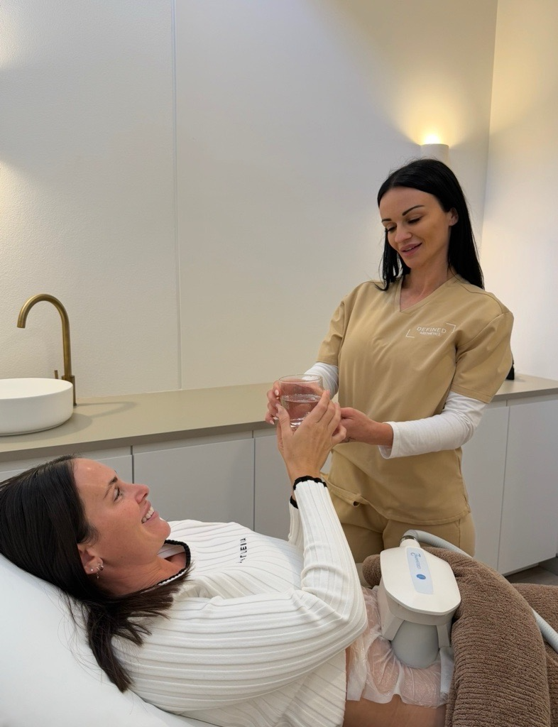 A smiling client receiving a glass of water from a Defined Aesthetics practitioner